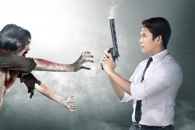 Empresario asiático con la pistola en la mano frente a los zombies