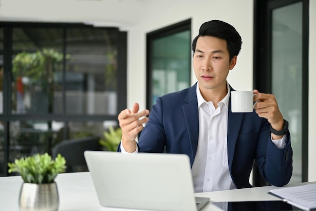 Empresário asiático profissional tomando café enquanto faz uma reunião online