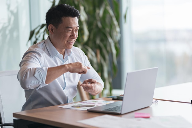 Empresário asiático se comunicando em videochamada com cliente surdo em seu local de trabalho
