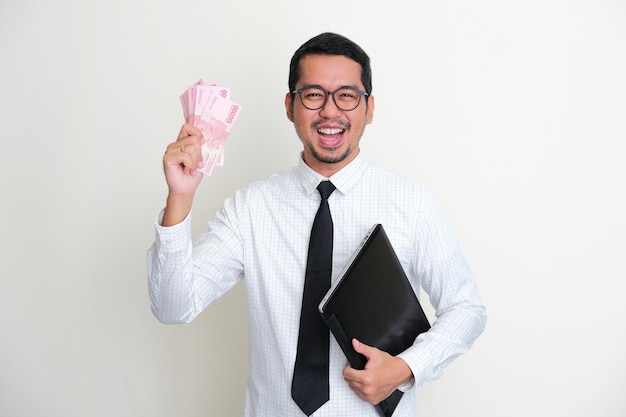 Empresário asiático segurando um laptop e papel-moeda mostrando expressão feliz