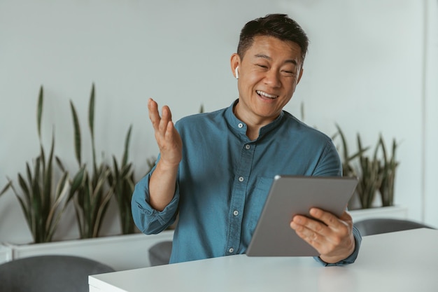 Empresario asiático sonriente haciendo videollamadas a un cliente sentado en un coworking moderno