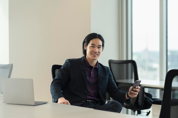 Un empresario asiático sonriente con un teléfono móvil trabajando en línea leyendo un mensaje de texto