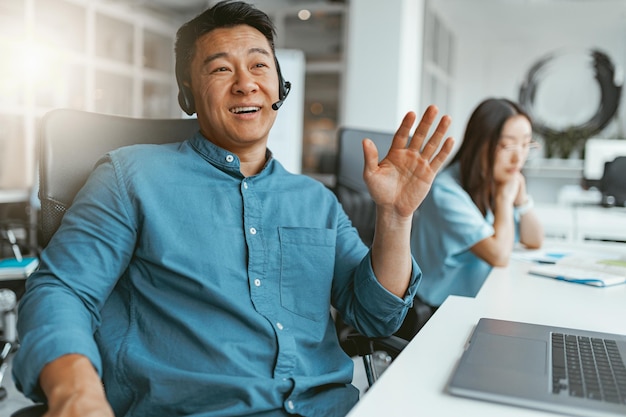 Empresário asiático sorridente falando ao telefone com o cliente enquanto está sentado no escritório no fundo do colega