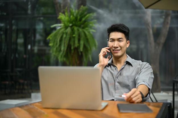 Empresário asiático sorridente sentado ao ar livre e falando ao telefone