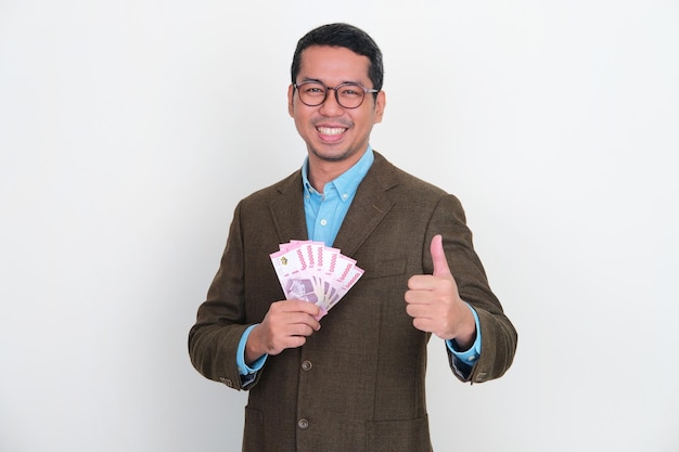 Empresário asiático sorrindo e dando o polegar para cima enquanto segura dinheiro