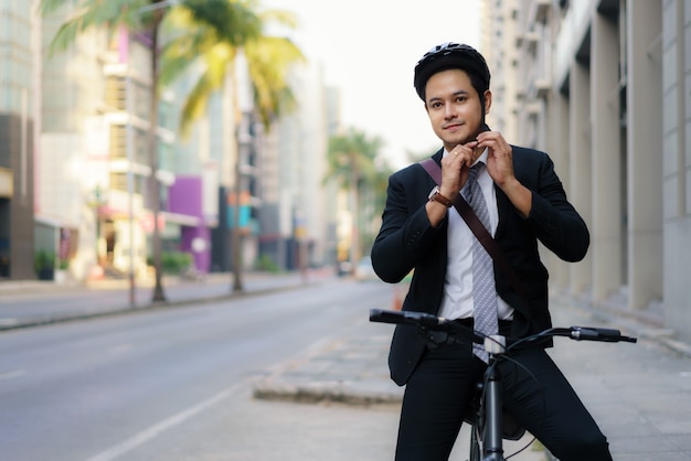 El empresario asiático en trajes lleva cascos de seguridad para andar en bicicleta por las calles de la ciudad