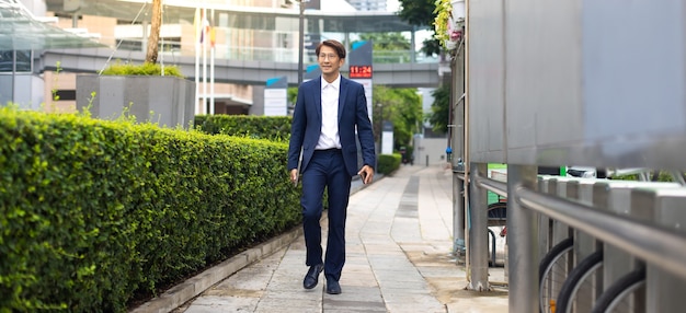 Empresário asiático vestindo paletó andando vai trabalhar de manhã ao ar livre.
