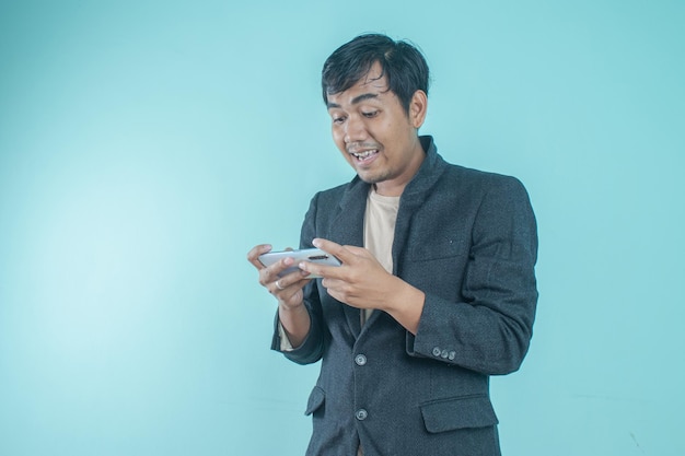 Empresário asiático vestindo terno preto parece feliz jogando com telefone inteligente. de pé em um azul b