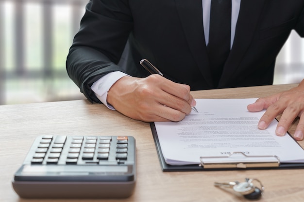 Empresário assinando contrato com chave e calculadora na mesa de madeira