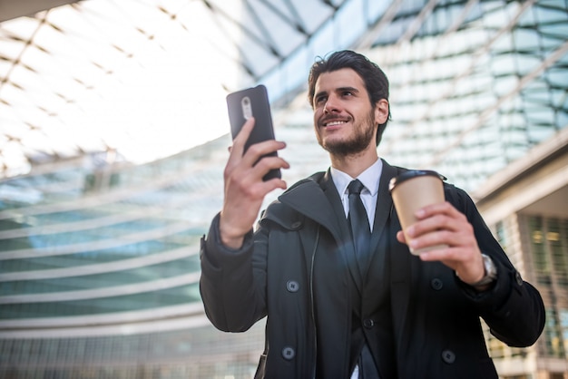 Empresário assistindo seu smartphone enquanto bebe um café