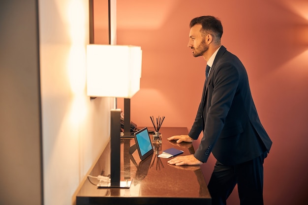 Empresario atractivo seguro poniendo las manos en la cómoda y mirando su reflejo en un espejo en la zona de salón de negocios