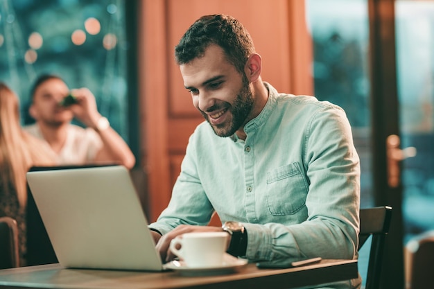 Empresário atraente usando um laptop e sorrindo enquanto trabalhava no café