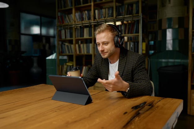 Empresario con auriculares sosteniendo una videoconferencia con socios sentados en una mesa de escritorio con una computadora portátil en la oficina. Reunión en línea, comunicación digital, concepto de sesión informativa de chat virtual