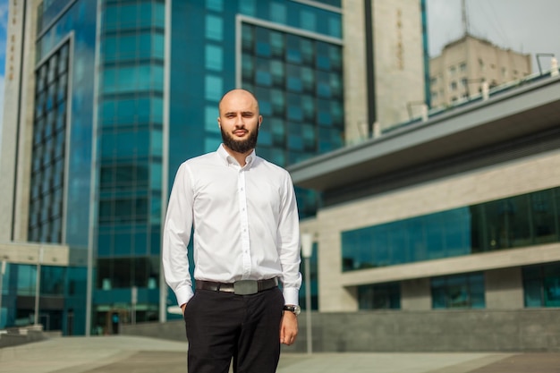 Empresario con barba en camisa blanca de pie cerca del edificio de oficinas