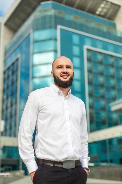 Empresario con barba en camisa blanca de pie cerca del edificio de oficinas