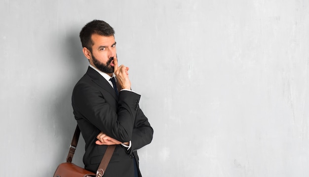 Empresario con barba mostrando un signo de cierre de boca y gesto de silencio