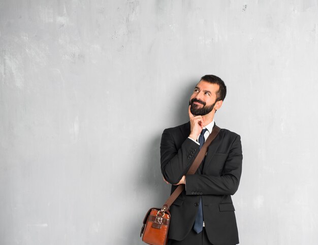 Empresario con barba de pie y pensando en una idea mientras mira hacia arriba