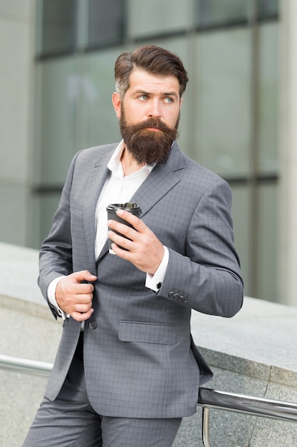 Empresário barbudo bebe café para viagem. homem formal em terno de escritório, bebendo café em um copo de papel. bom dia café. tirar bebida. empresário confiante precisa de inspiração.