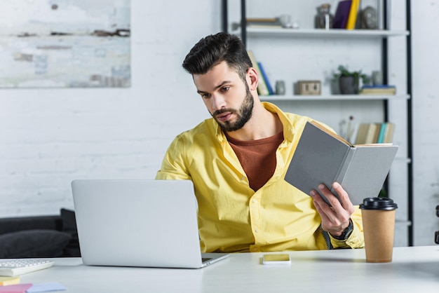 Empresário barbudo concentrado olhando para laptop e segurando o livro