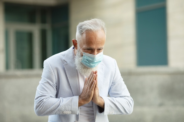 Empresario barbudo con mascarilla y saludo con namaste para prevenir la propagación del virus