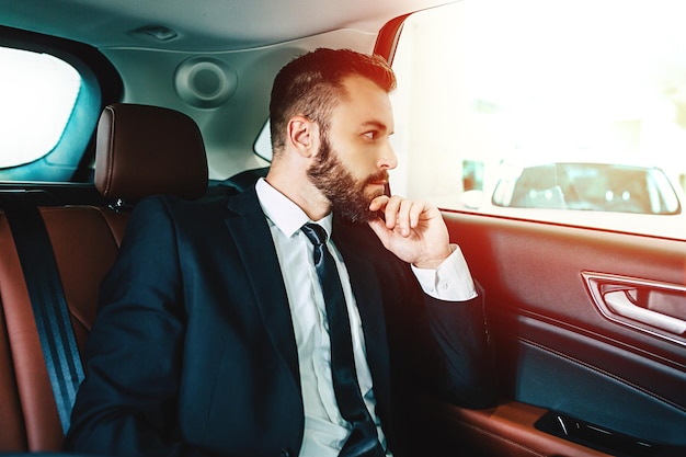 Empresario barbudo pensativo en taxi mirando por la ventana del coche