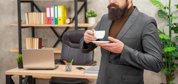 Empresário barbudo recortado tomando café no escritório com espaço de cópia de manhã