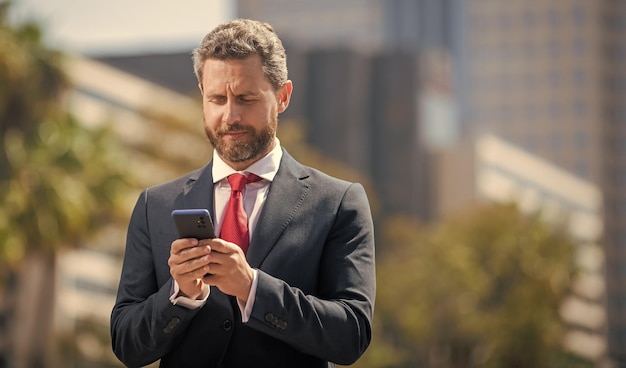 Empresario barbudo en ropa formal chateando en un teléfono inteligente fuera de la comunicación de la oficina