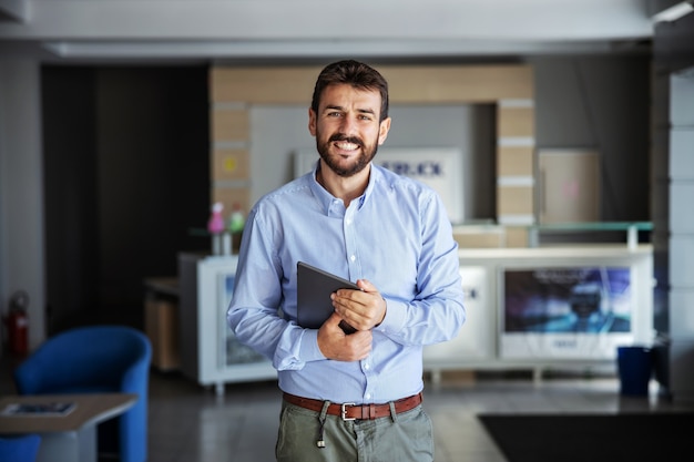 Empresário barbudo sorridente no saguão da empresa de navegação e segurando o tablet. a entrega é sempre pontual.