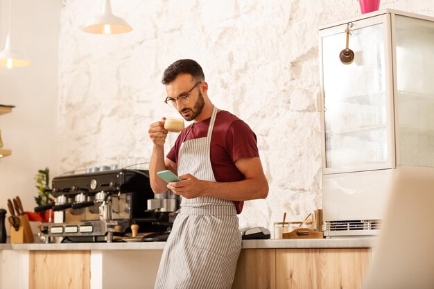 Empresario bebiendo café y leyendo mensajes en el teléfono inteligente