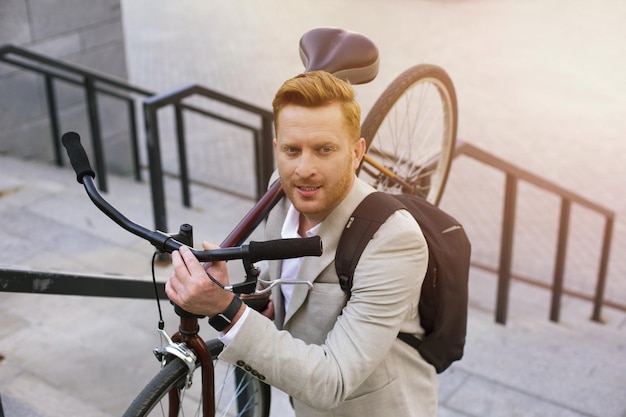 Empresário bonito ativo subindo com uma bicicleta nas mãos