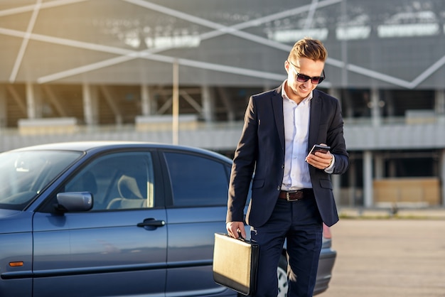 Empresário bonito atraente com diplomata e smartphone nas mãos perto do carro