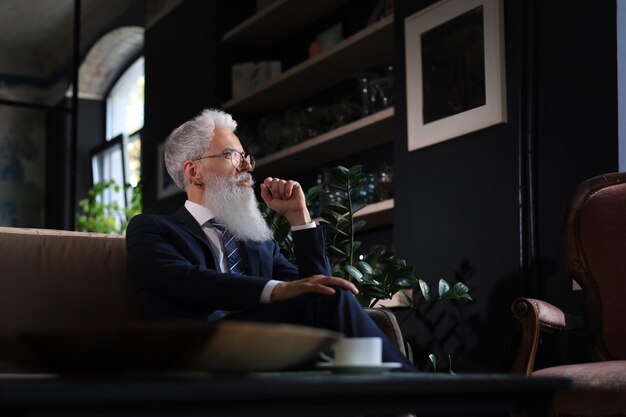 Empresário bonito confiante pensativo pensando enquanto está sentado no sofá em seu escritório moderno sobre o conceito de negócios coffee break