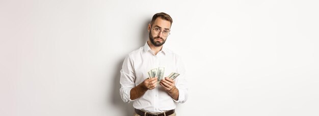 Empresário bonito contando dinheiro e olhando para a câmera séria contra o fundo branco