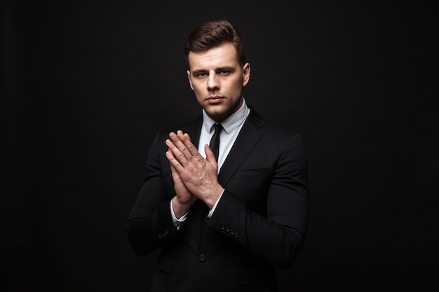 Empresário bonito e confiante vestindo terno isolado na parede preta, posando