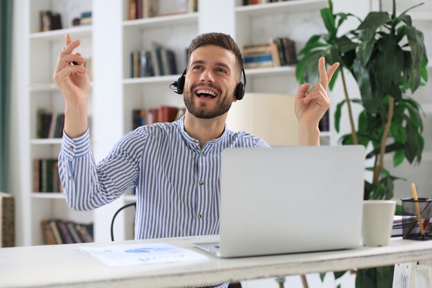 Empresário bonito está mantendo os braços levantados e expressando alegria no escritório.