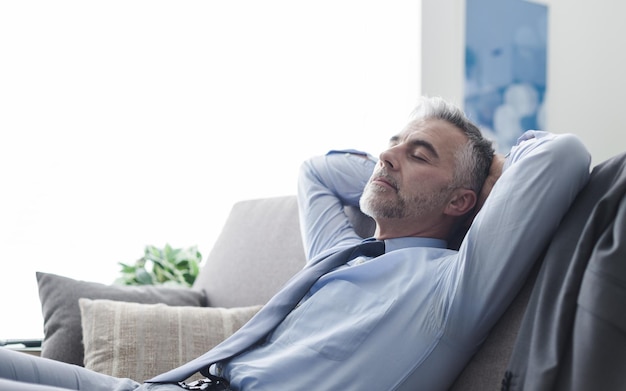 Empresário bonito relaxando em casa no sofá, ele está dormindo com as mãos atrás da cabeça