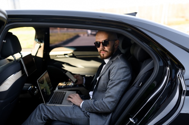 Empresário bonito sentado com o laptop no banco de trás do carro. viajando de carro e trabalhando no laptop