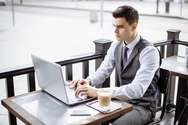 Empresário bonito vestindo terno e usando laptop moderno ao ar livre