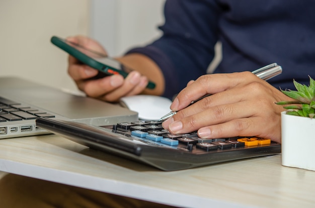 El empresario con una calculadora tiene un lápiz y un teléfono móvil en un escritorio con una computadora portátil trabajando desde casa.