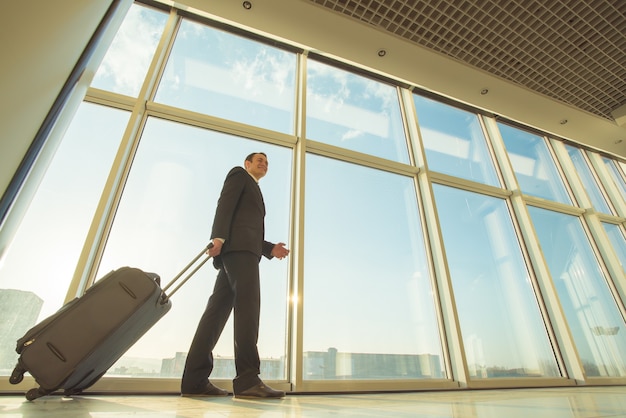 El empresario camina con una maleta cerca de ventanas panorámicas.