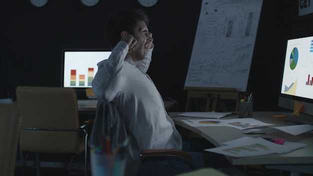 Empresario cansado estirándose y bostezando cerca de la computadora en la oficina nocturna