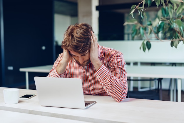 Empresário cansado, trabalhando em seu computador no escritório de espaço aberto. Fim do dia útil