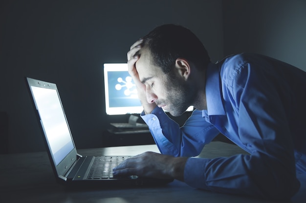 Empresario cansado usando una computadora portátil en su escritorio por la noche