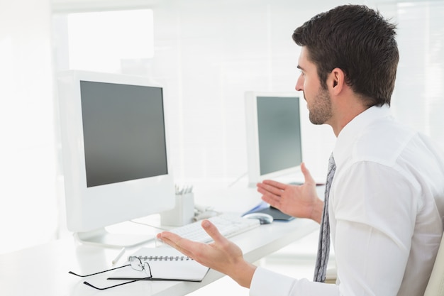 Empresário carrancudo gesticulando na frente de seu computador