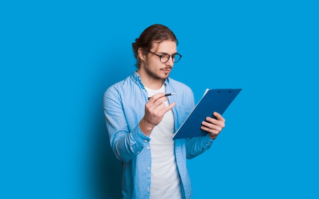 Foto empresário caucasiano confiante vestido de azul está fazendo alguns avisos em seu bloco de notas enquanto posa sobre um fundo azul