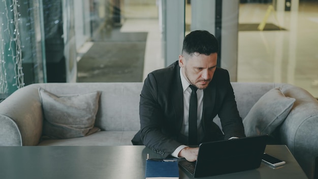 Empresário caucasiano em terno de negócios preto sentado e trabalhando concentrado em seu computador portátil