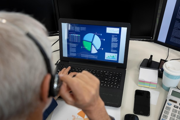 Foto empresário caucasiano trabalhando em um escritório moderno, sentado à mesa com o computador, usando fone de ouvido e laptop. distanciamento social no local de trabalho durante a pandemia do coronavirus covid 19.