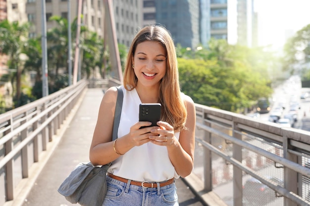 Empresario caucásico brasileño caminando en el centro de Sao Paulo enviando mensajes con un teléfono celular