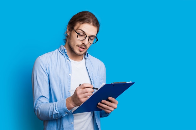 Empresario caucásico concentrado está escribiendo algo en una carpeta posando en un azul con psace gratis