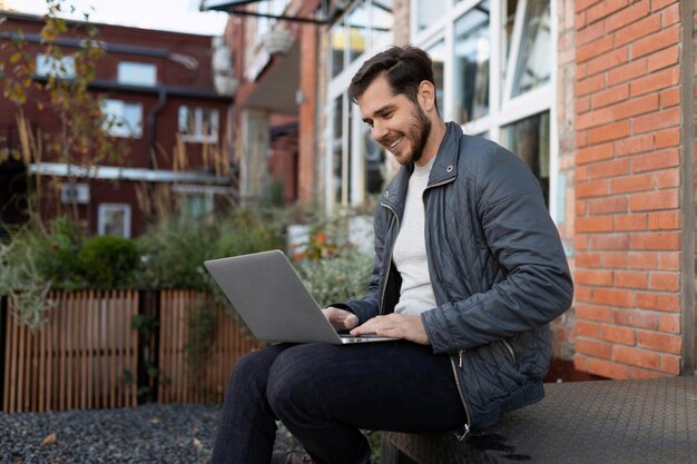 Empresario celebrando una reunión en línea sentado de forma remota en una computadora portátil en la calle